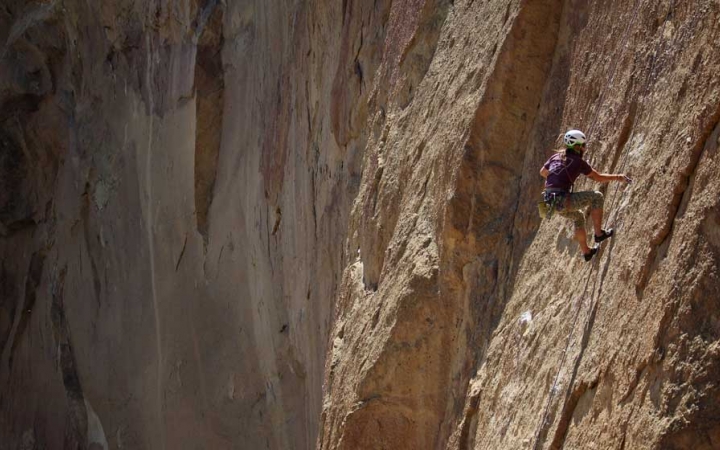 Wearing safety gear and secured by ropes, a person climbs a steep rock wall.